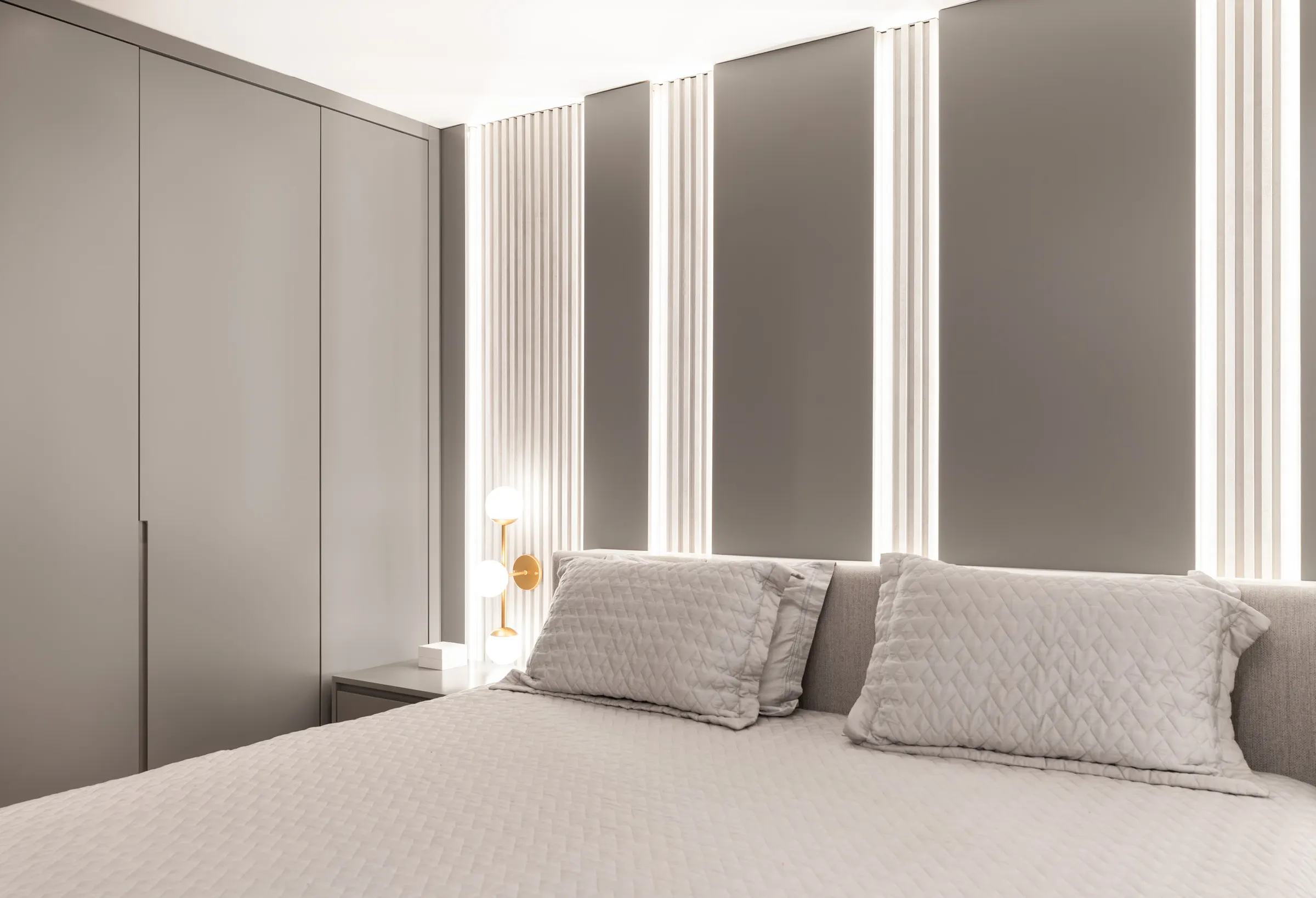 Dormitório com painel ripado iluminado atrás da cama e armário embutido